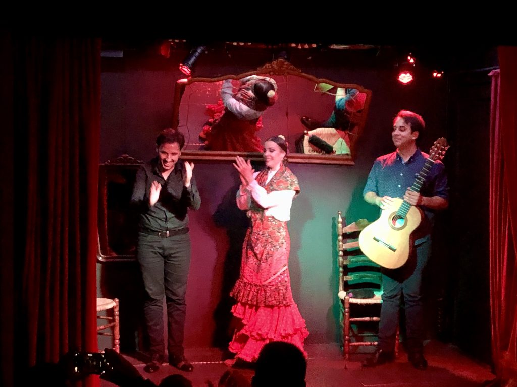 Flemenco show in Granada, Spain. A woman is dancing on stage. Two men in the backgound, one is playing the guitar and one is singing.