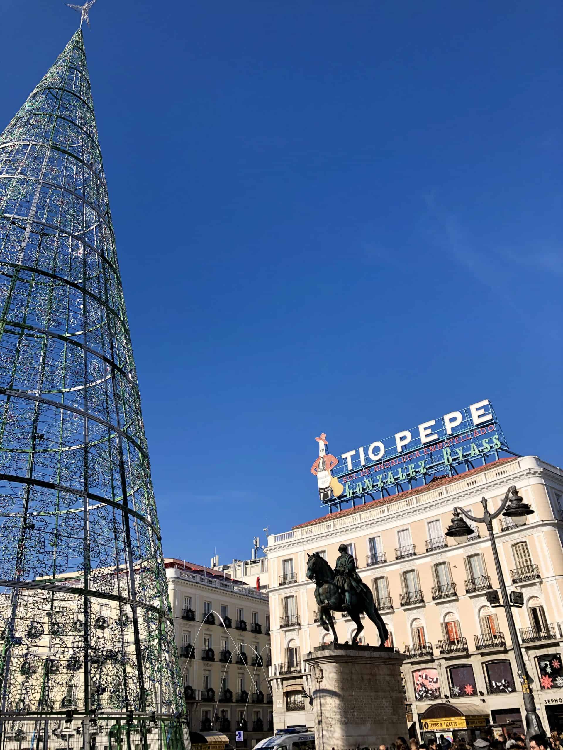 Puerta del Sol in Madrid, Spain in winter. Huge Christmas Tree in the middle of the square. Bronze statue of Carlos III with the Tio Pepe sign behind.
